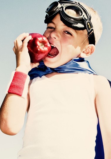 Young boy in superhero gear biting a red apple