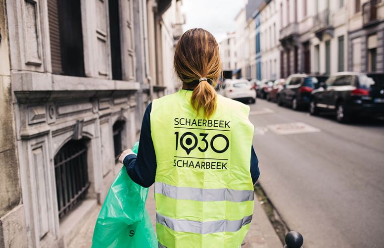 Person collecting rubbish on Schaerbeek streets wearing campaign jacket.