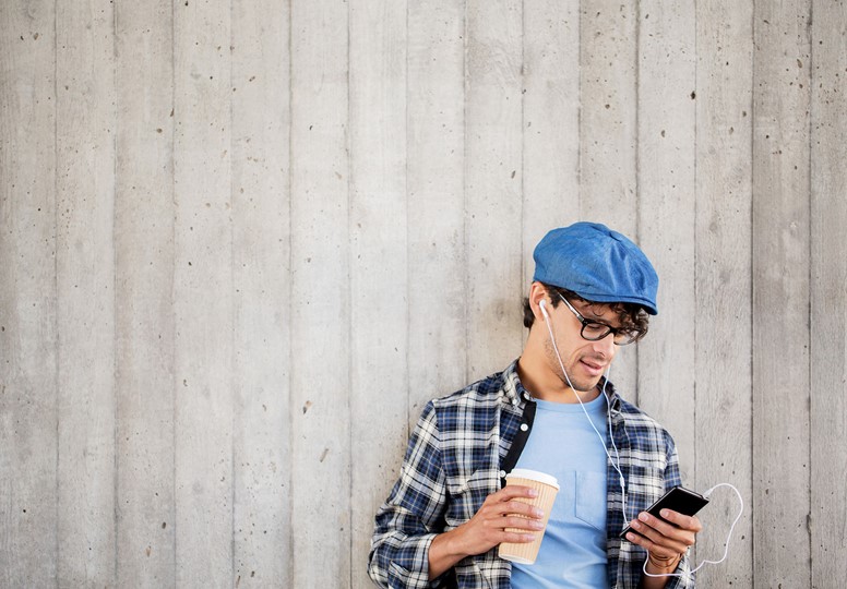 Young man in blue hat holding coffee and phone listening to a podcast