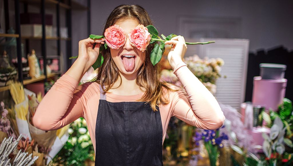Young female florist with flowers in front of eyes.
