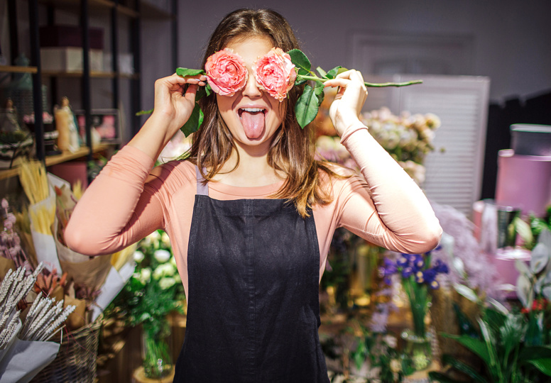 Young female florist with flowers in front of eyes.