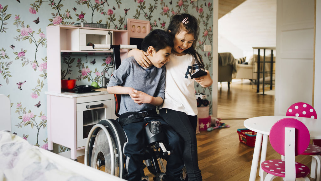Together for Rights Young girl hugging a boy in a wheelchair, both looking at a mobile phone