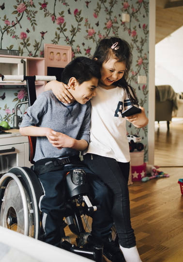 Together for Rights Young girl hugging a boy in a wheelchair, both looking at a mobile phone