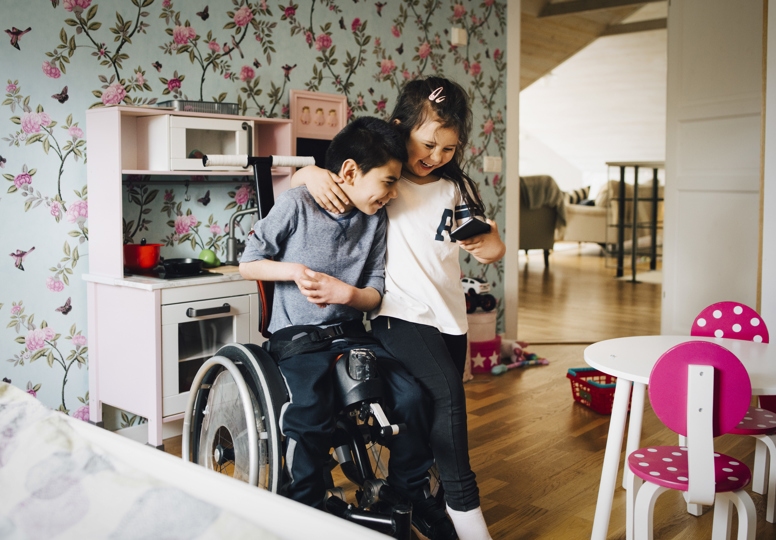 Together for Rights Young girl hugging a boy in a wheelchair, both looking at a mobile phone