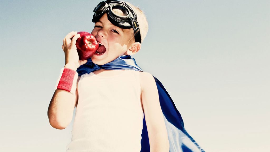 Bringing training results to life Young boy in superhero gear biting a red apple