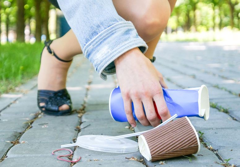 Female hands picking up trash outdoors in the street in summer