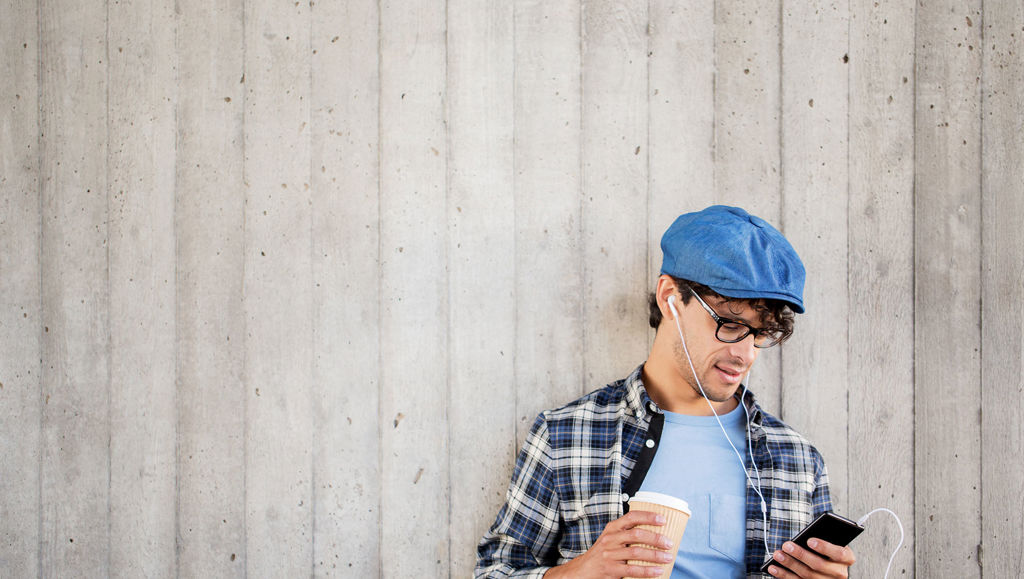 Young man in blue hat holding coffee and phone listening to a podcast