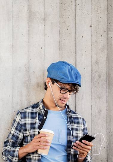Young man in blue hat holding coffee and phone listening to a podcast