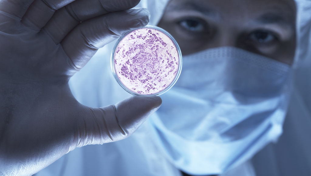 Man in protective lab gear holding petri dish