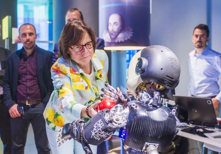 Group of men watching a woman interact with a robot