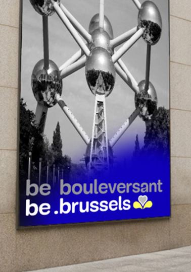 ‘be.brussels’— a platform that gives the population a voice Lady walking past photo of Atomium on a wall. Man talking behind rostrum