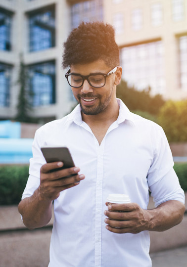 Young handsome Afro American man standing in front of huge modern business building smiling and talking on cell phone