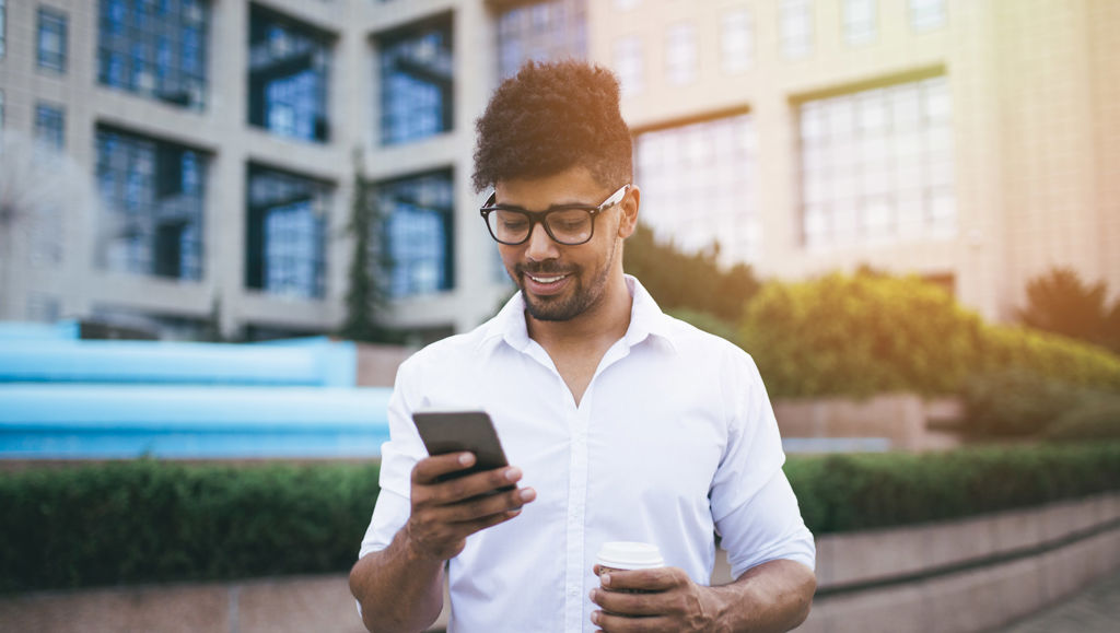 The EU’s ‘What’s on?’ Young handsome Afro American man standing in front of huge modern business building smiling and talking on cell phone