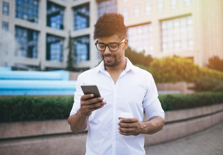 The EU’s ‘What’s on?’ Young handsome Afro American man standing in front of huge modern business building smiling and talking on cell phone