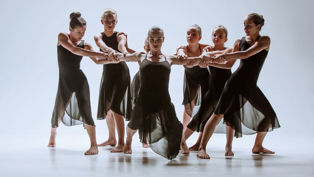 The group of modern ballet dancers dancing on gray studio background