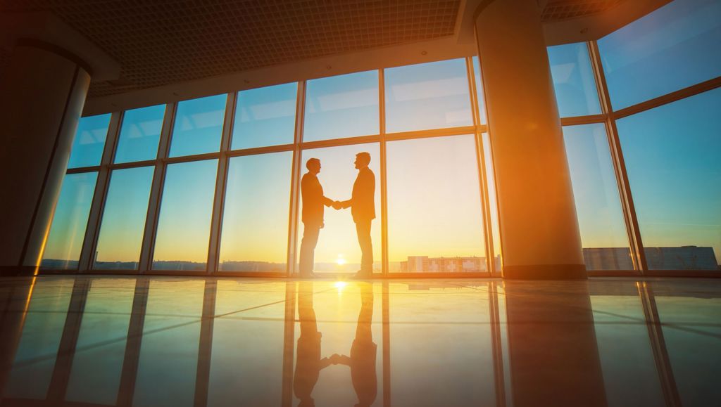 Two businessmen handshake in the office on the bright sun background