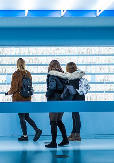 Three young girls looking at hundreds of images of faces on a wall