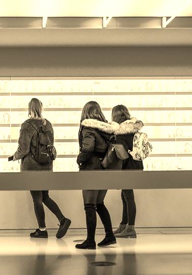 Three young girls looking at hundreds of images of faces on a wall
